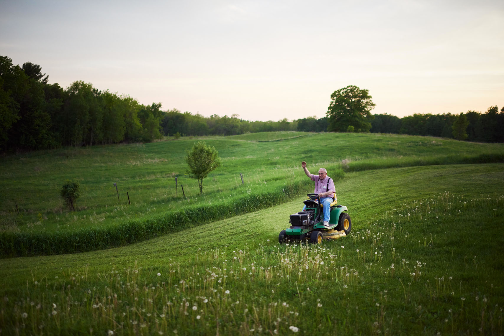 Old man waves hello from riding lawn mower