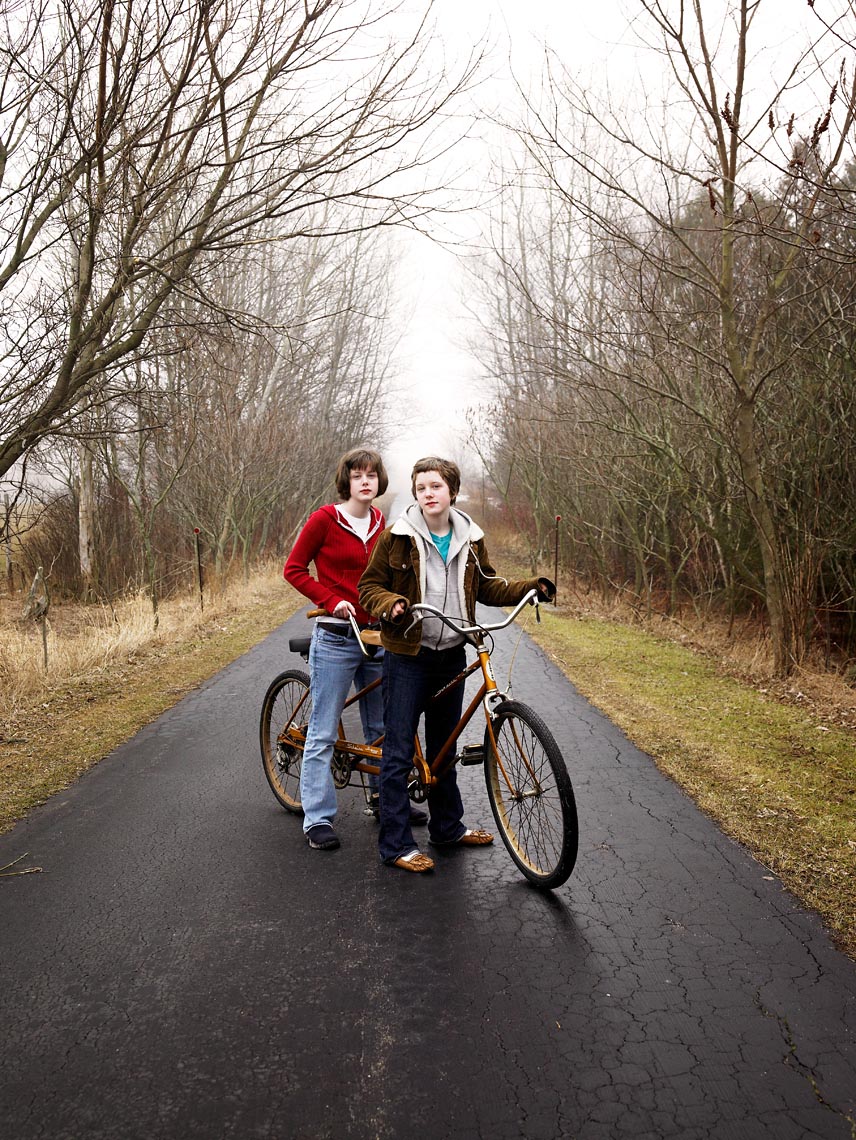 Twins with tandem bicycle on driveway portrait