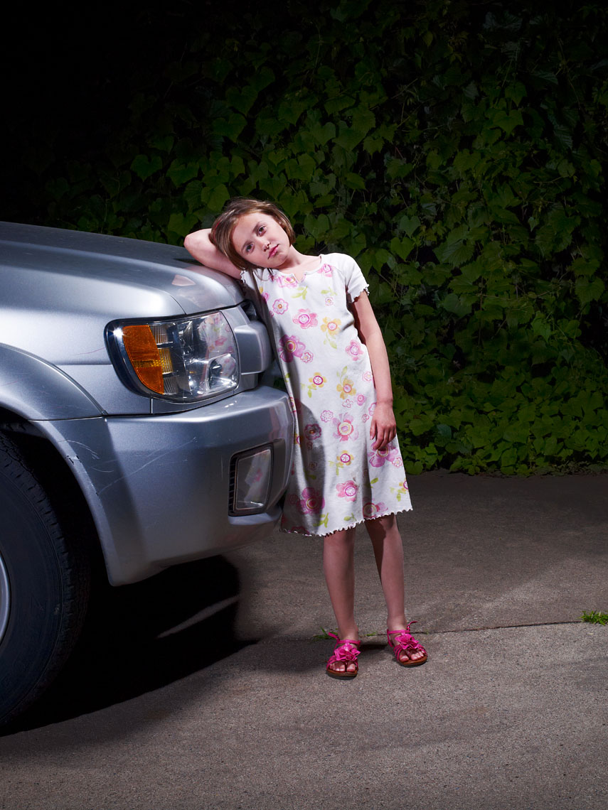 Young girl leans on SUV in driveway portrait