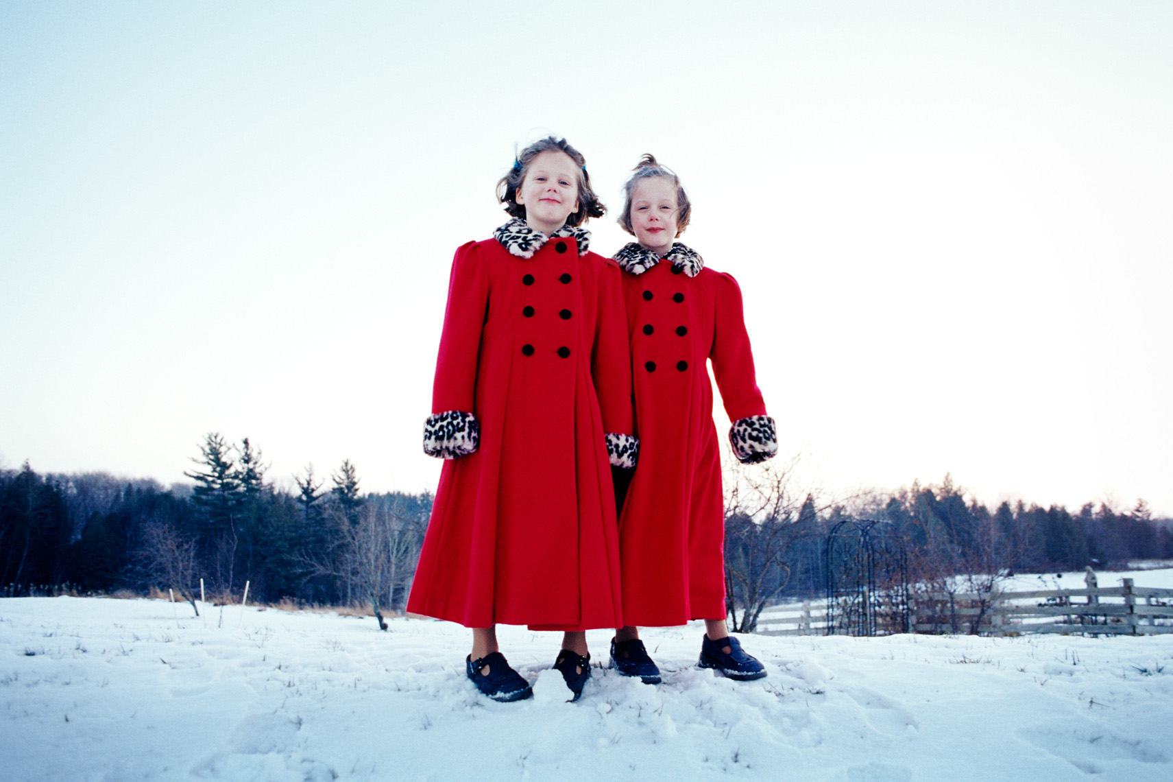 Young twin girls in snow with matching red coats portrait